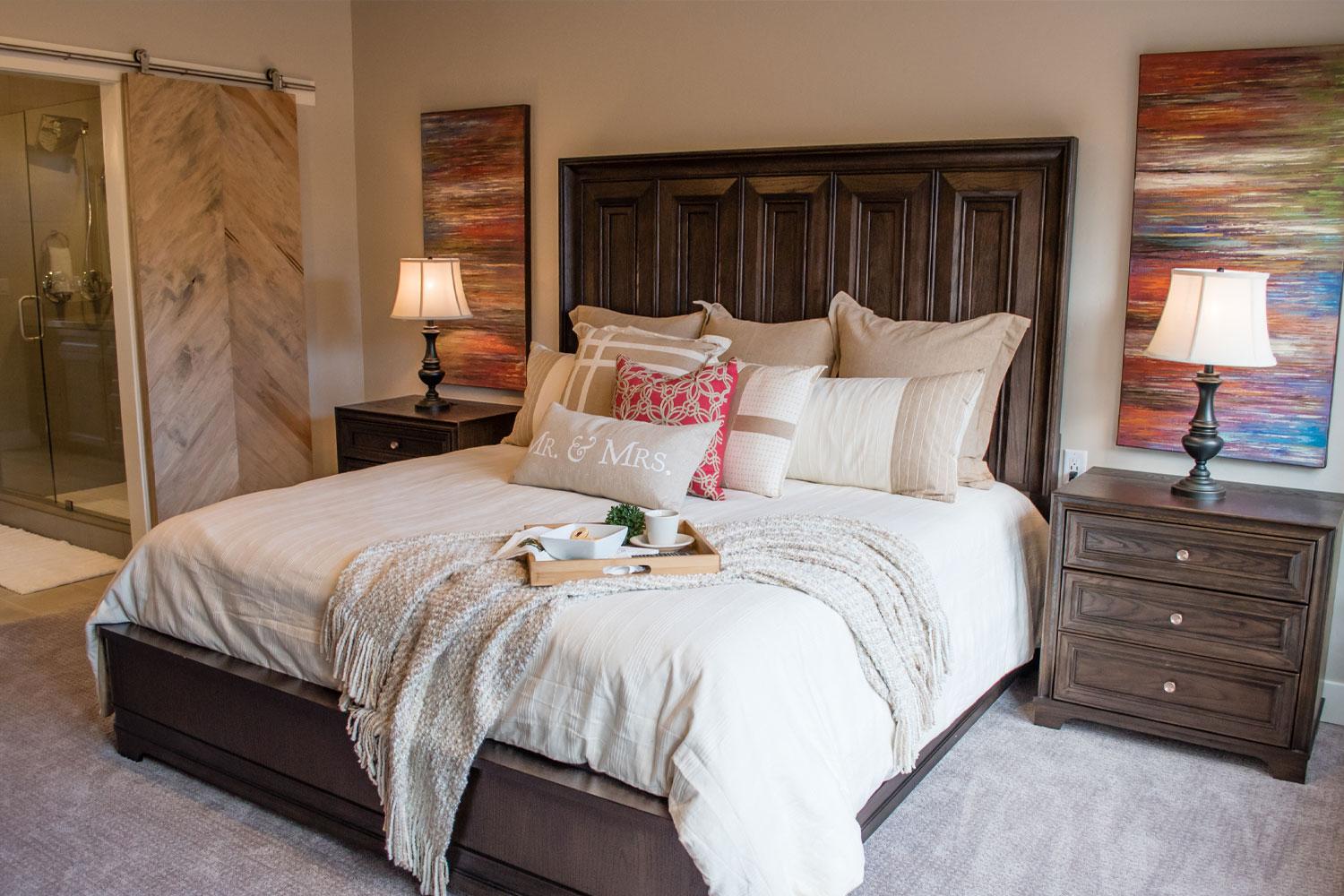 master bedroom, two side tables and lamps, soft grey carpet, beige bedspread and throw blanket, entrance to bathroom