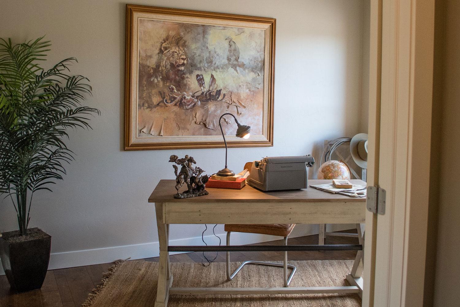 office room with large painting on the wall, one small desk and chair and desk lamp, area rug on the floor