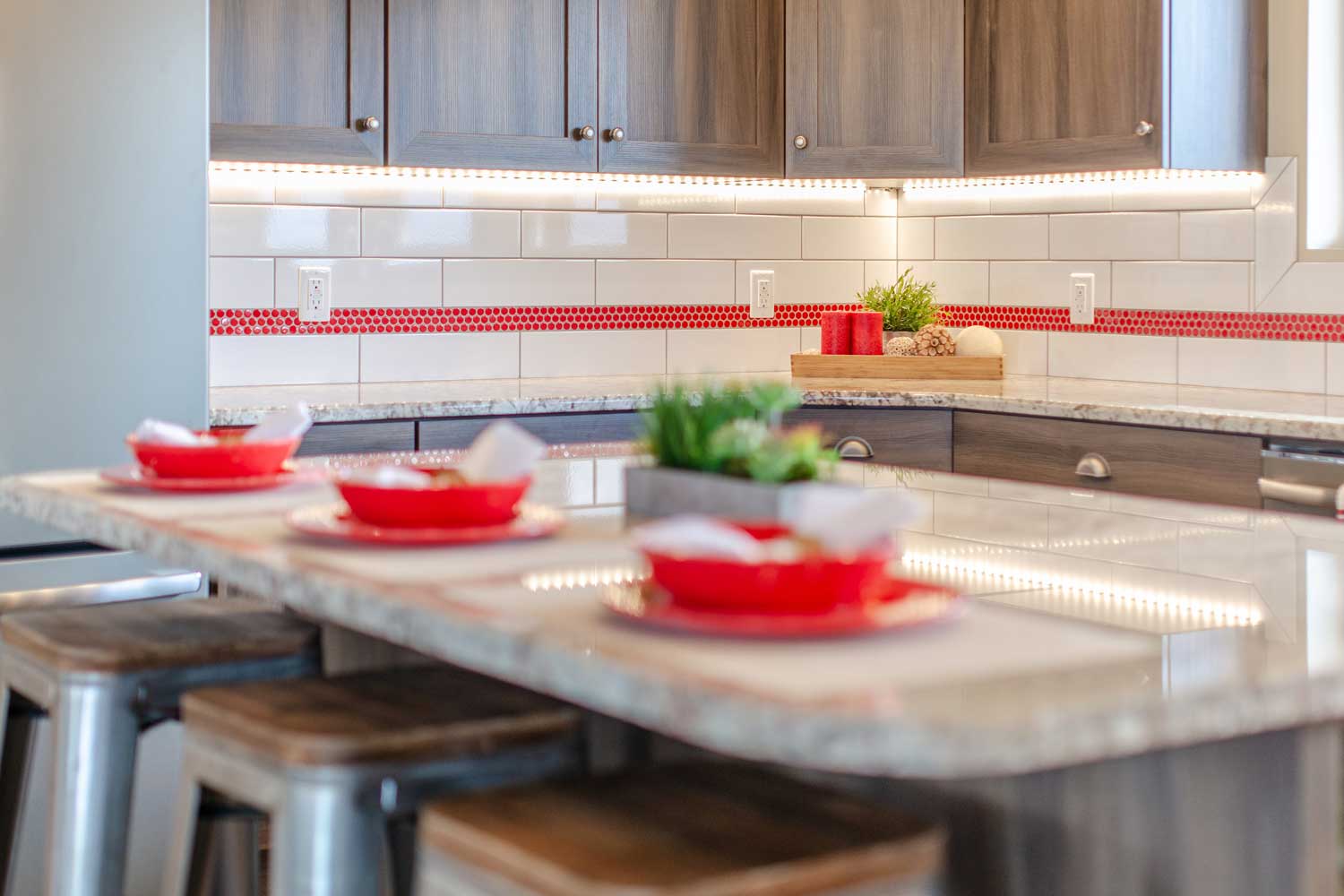 kitchen counter bar area with three bar stools made of silver metal and wood seats, red bowls and white linens