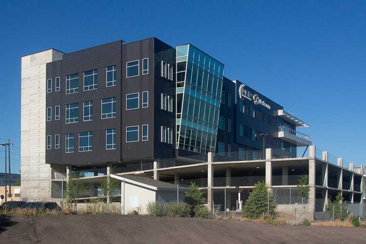 Modern multi-story office building with large glass windows and dark exterior panels under a clear blue sky.