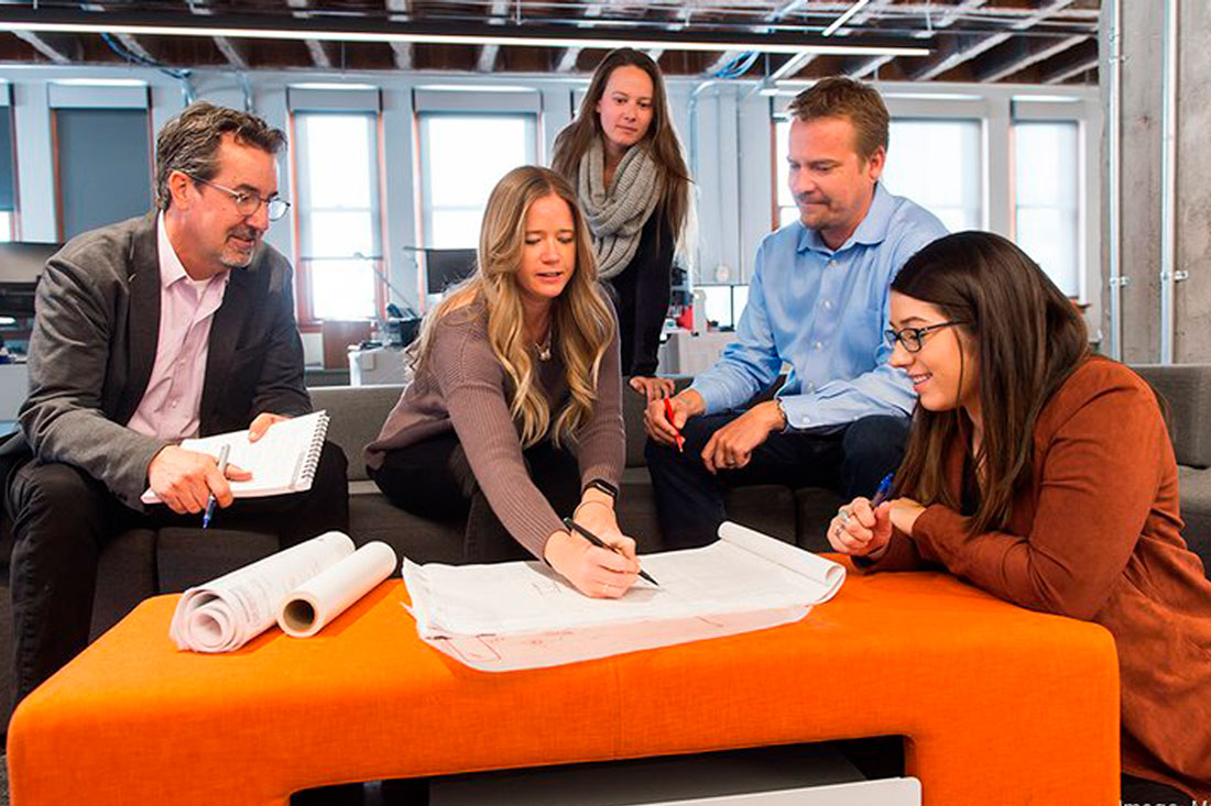 Five MOA ARCHITECTURE team members reviewing building plans.