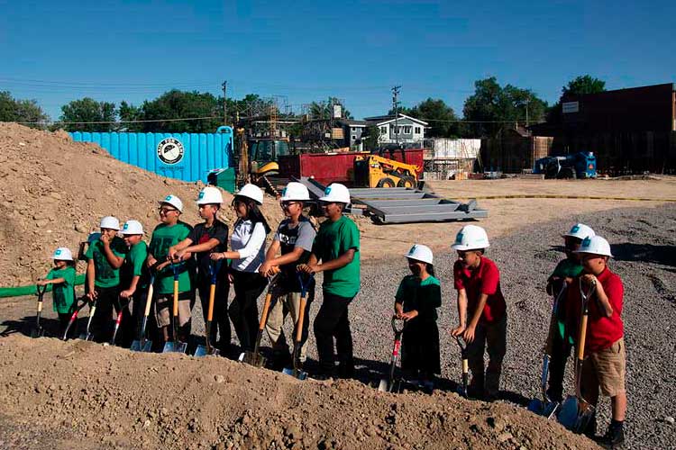 A group of young students shoveling dirt in a groundbreaking ceremony.