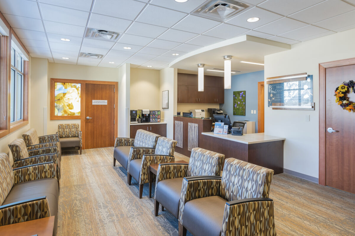 Waiting area with patterned upholstered chairs, carpet flooring, wood doors with decorative glass panels, framed artwork, a reception desk with pendant lighting, and built-in cabinetry along the back wall.