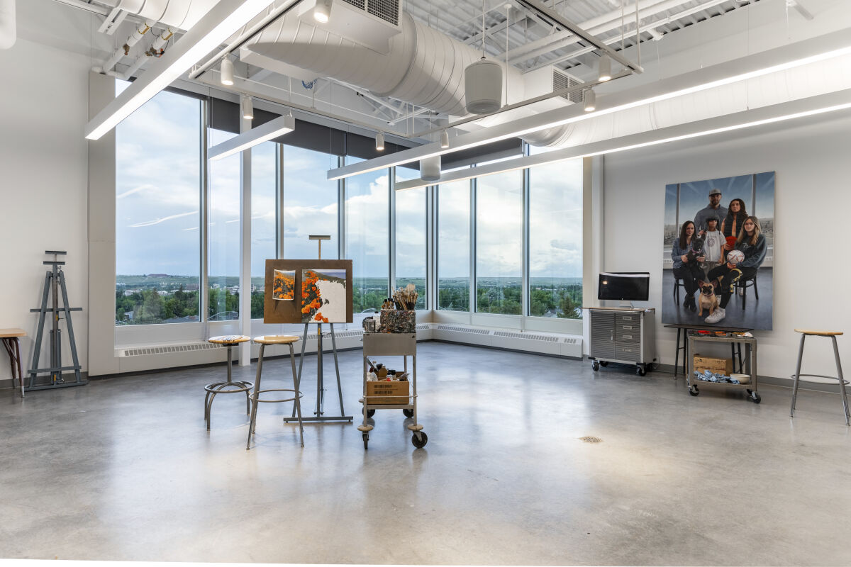 Art studio in the Casper College Tobin Visual Arts Center with large floor‑to‑ceiling windows, easels, rolling carts, stools, exposed ductwork, and polished concrete flooring.
