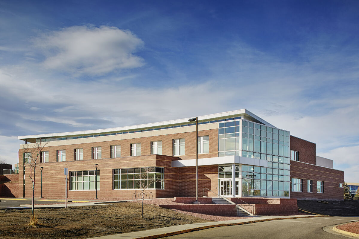 Casper College Music Building with a two‑story brick structure, a glass‑fronted corner entry volume, horizontal window bands, metal canopy elements, and landscaped walkways surrounding the building.