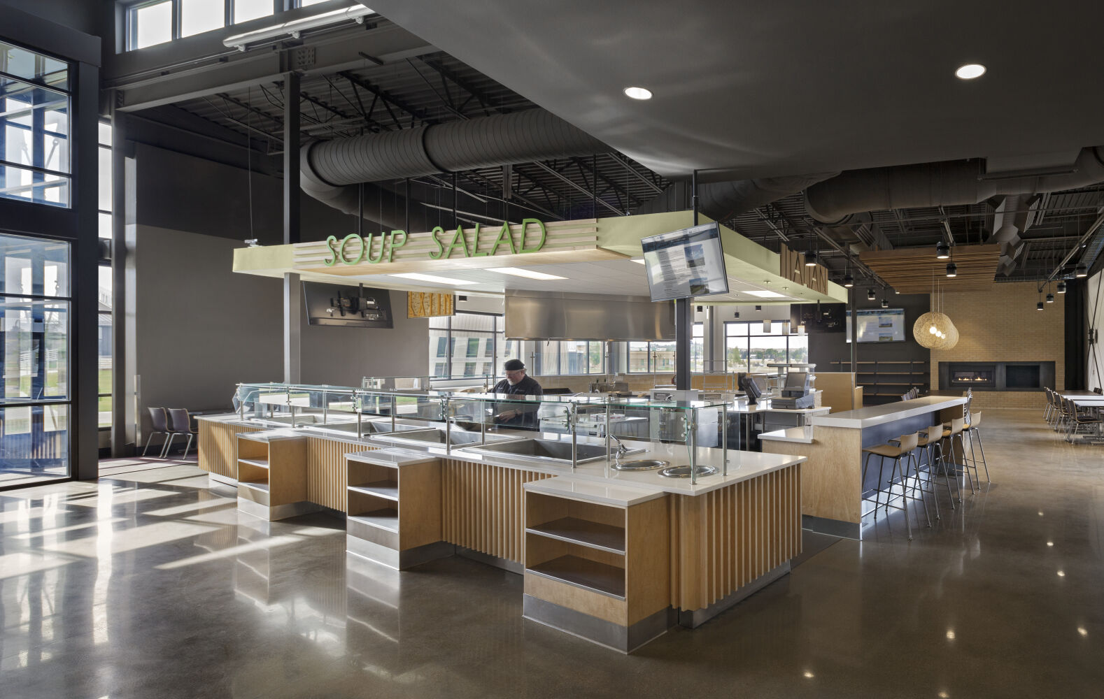 Food service counter at Gillette College with glass sneeze guards, wood finishes, overhead signage, and polished concrete flooring.