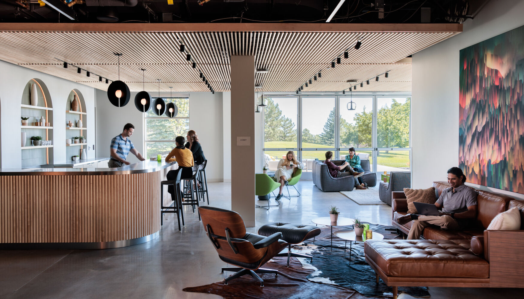 Interior lounge at Infinite Labs with a wood slat ceiling, bar‑height counter, soft seating, large windows, and integrated shelving.