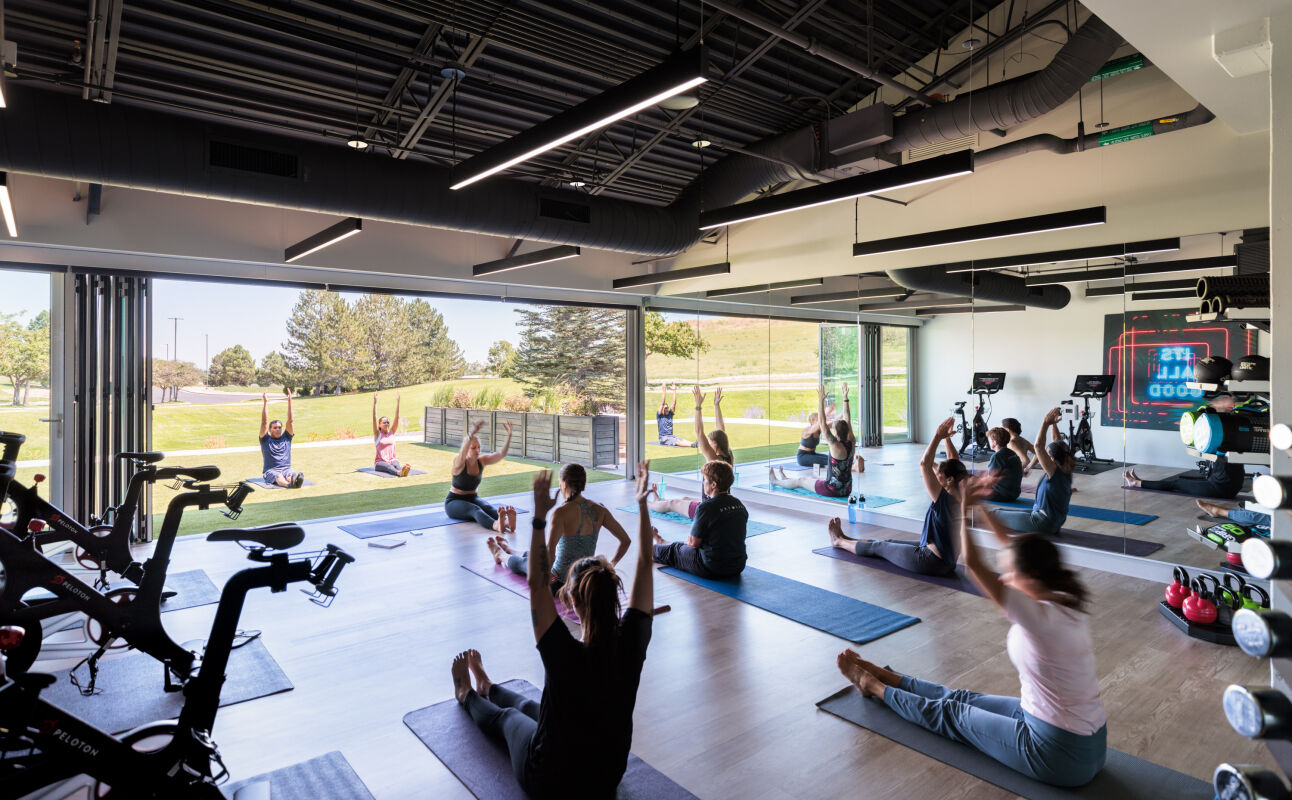 Movement studio at Infinite Labs with exercise mats, wood flooring, fitness equipment, and large operable glass walls opening to the lawn.