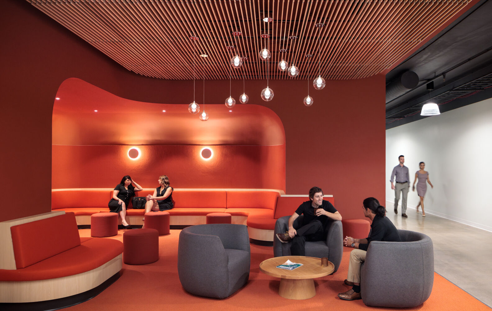 Interior lounge at Infinite Labs with curved upholstered seating, pendant lights, a wood slat ceiling, and warm accent walls.
