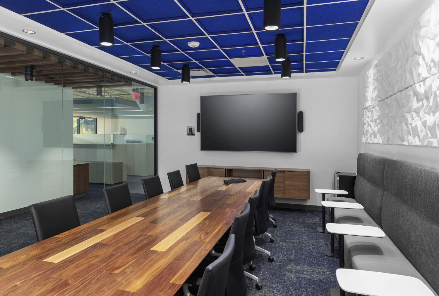 Conference room at Cogent Biosciences with a long wood table, wall‑mounted display, upholstered bench seating, and acoustic ceiling panels.