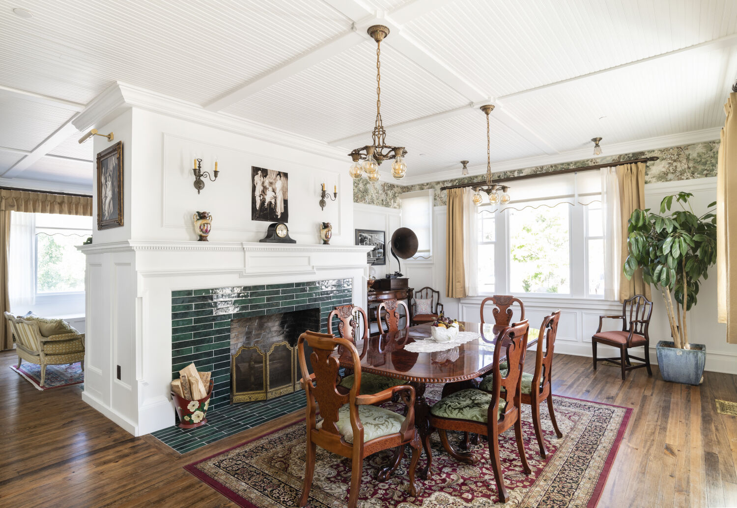 Dining room in the Stanley Caretaker’s Cottage with a wood dining table, carved chairs, tiled fireplace, period lighting, and hardwood flooring.