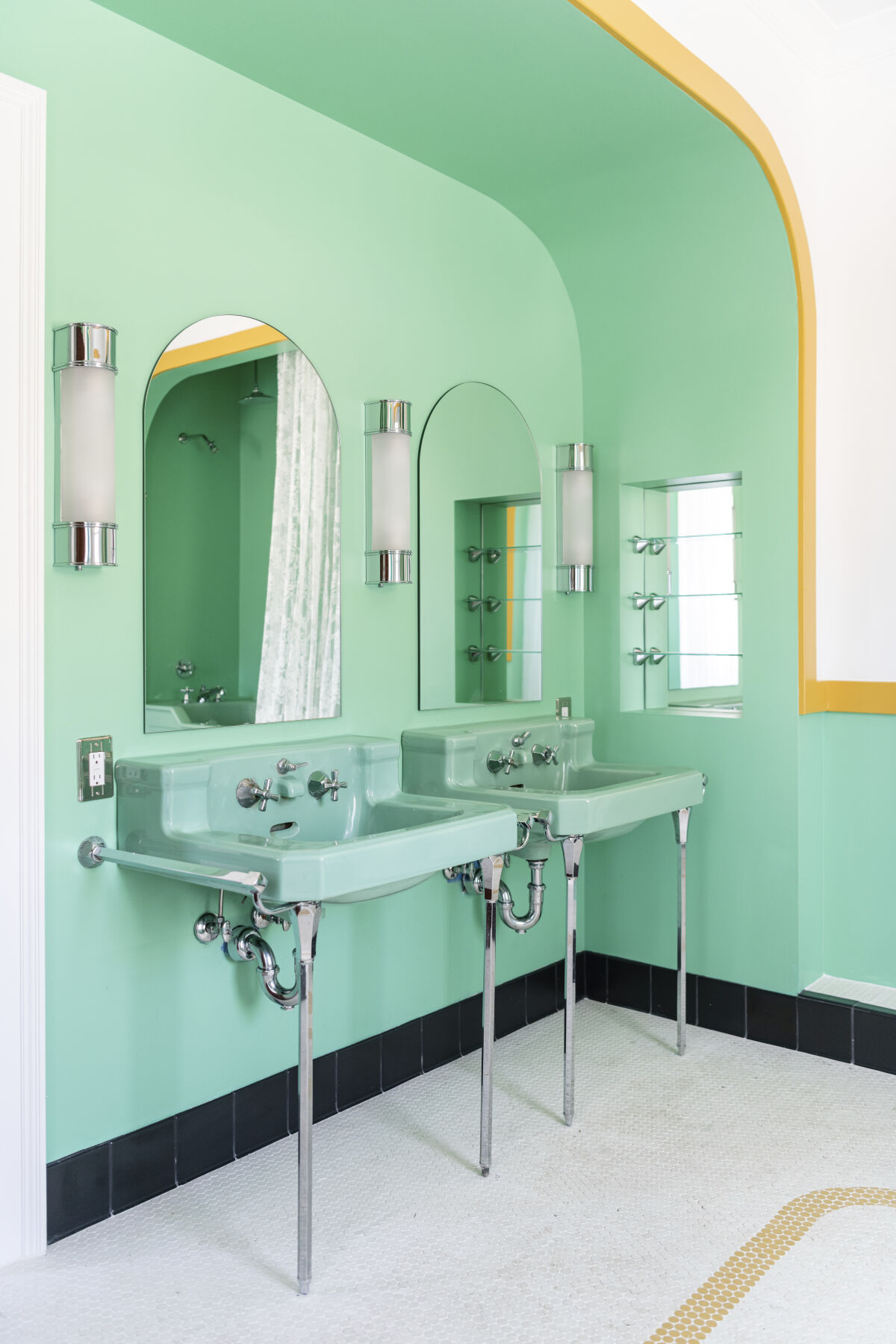 Bathroom in the Stanley Caretaker’s Cottage with dual green sinks, arched mirrors, wall sconces, and black tile trim.
