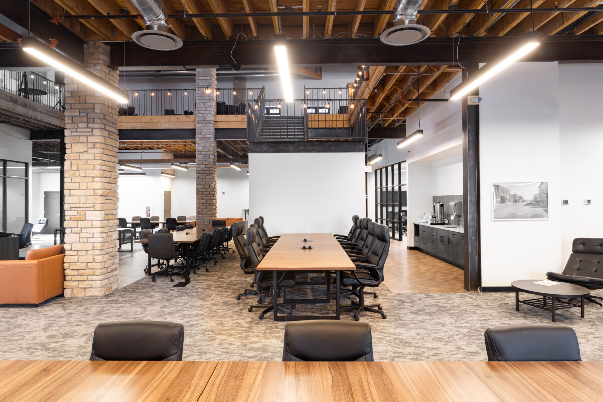 Casper Citiwerks coworking space with large conference tables, rolling office chairs, exposed wood ceilings, brick columns, and an open mezzanine level.