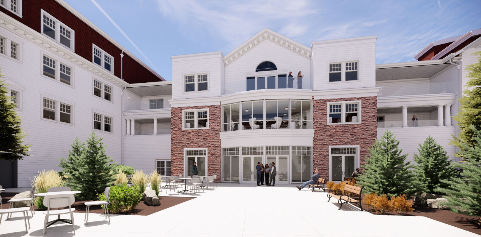 A landscaped courtyard framed by a white building with brick accents, large windows, upper‑level balconies, outdoor seating, and paved walkways connecting the surrounding wings.