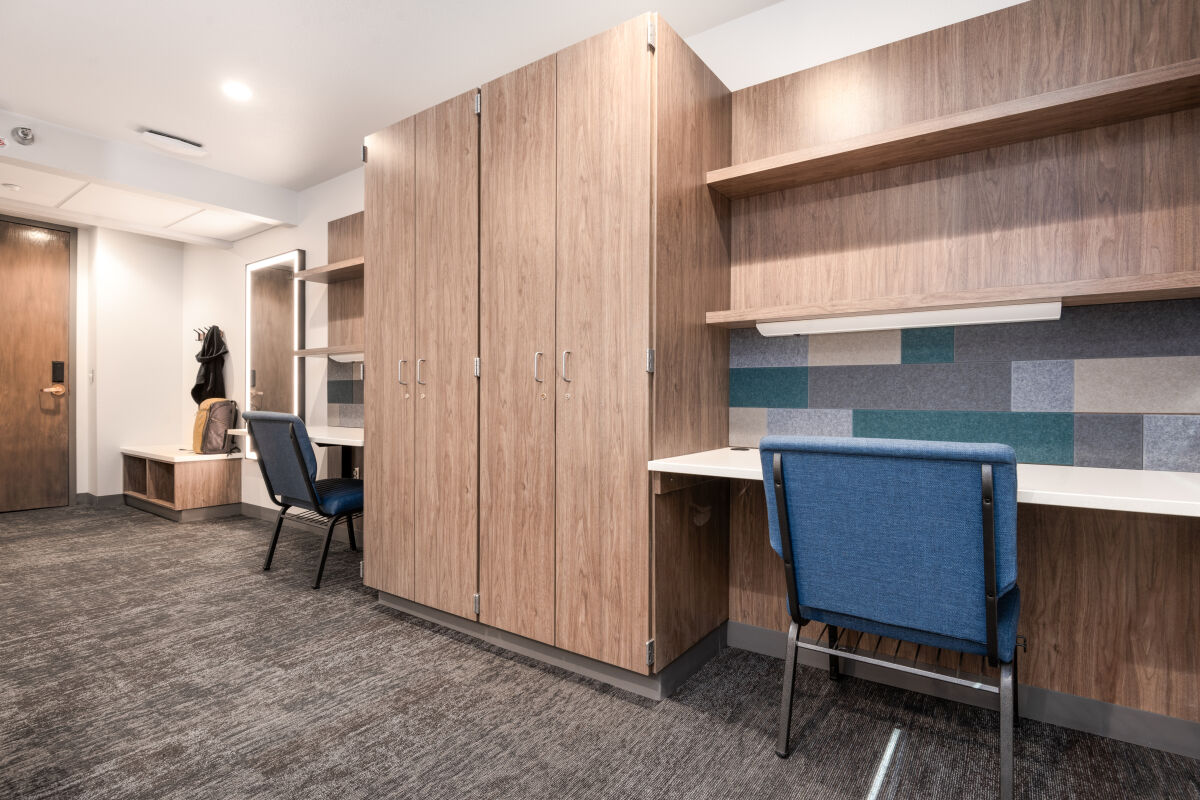 A dorm room layout with built‑in wardrobes, study desks, open shelving, acoustic wall panels, and task chairs arranged along a shared wall.