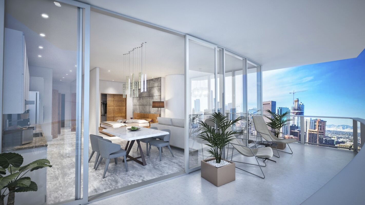 A residential unit with a glass wall opening from the dining and living area to a covered balcony furnished with lounge chairs and planters, creating an extended indoor‑outdoor living space.
