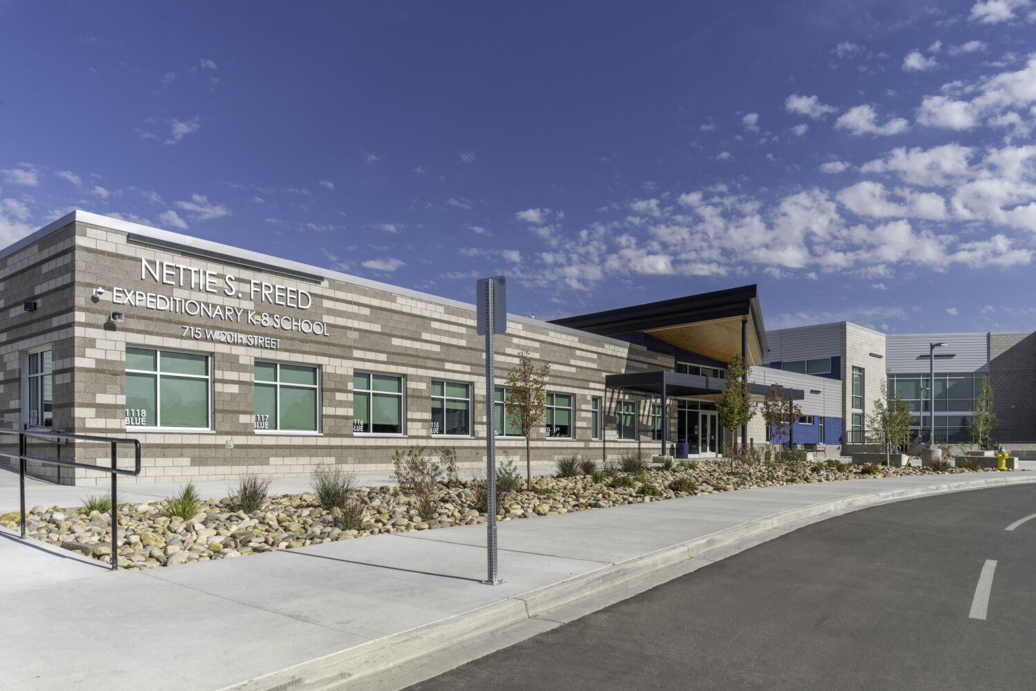 Nettie S. Freed Expeditionary K–8 School with a brick facade, glazed main entrance, wood‑accent canopy, and landscaped walkway along the front of the building.