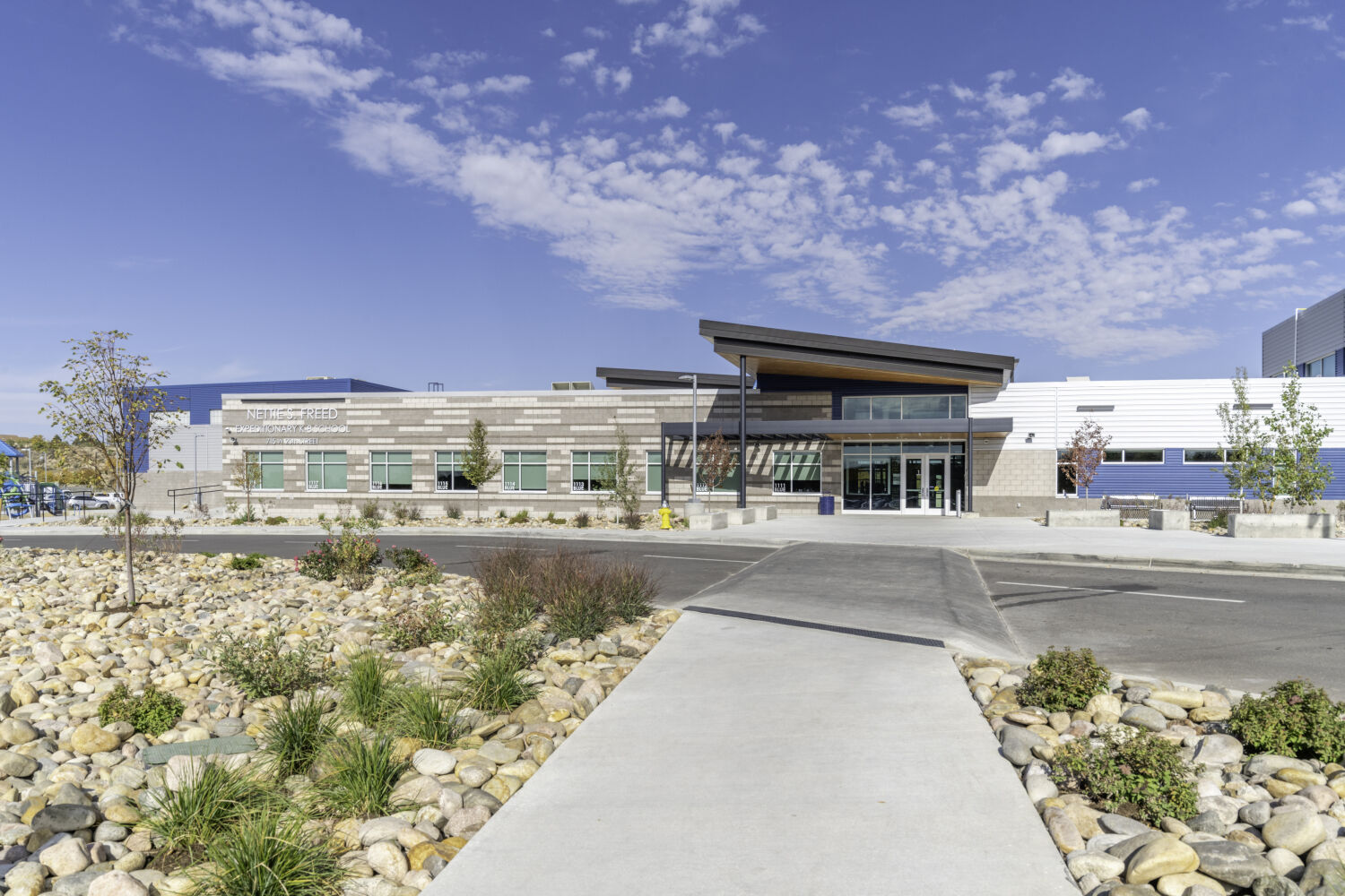 Main entrance of Nettie S. Freed K–8 Expeditionary School with a low‑profile building, glazed entry, wood‑accent canopy, mixed masonry and metal cladding, and landscaped approach walk.