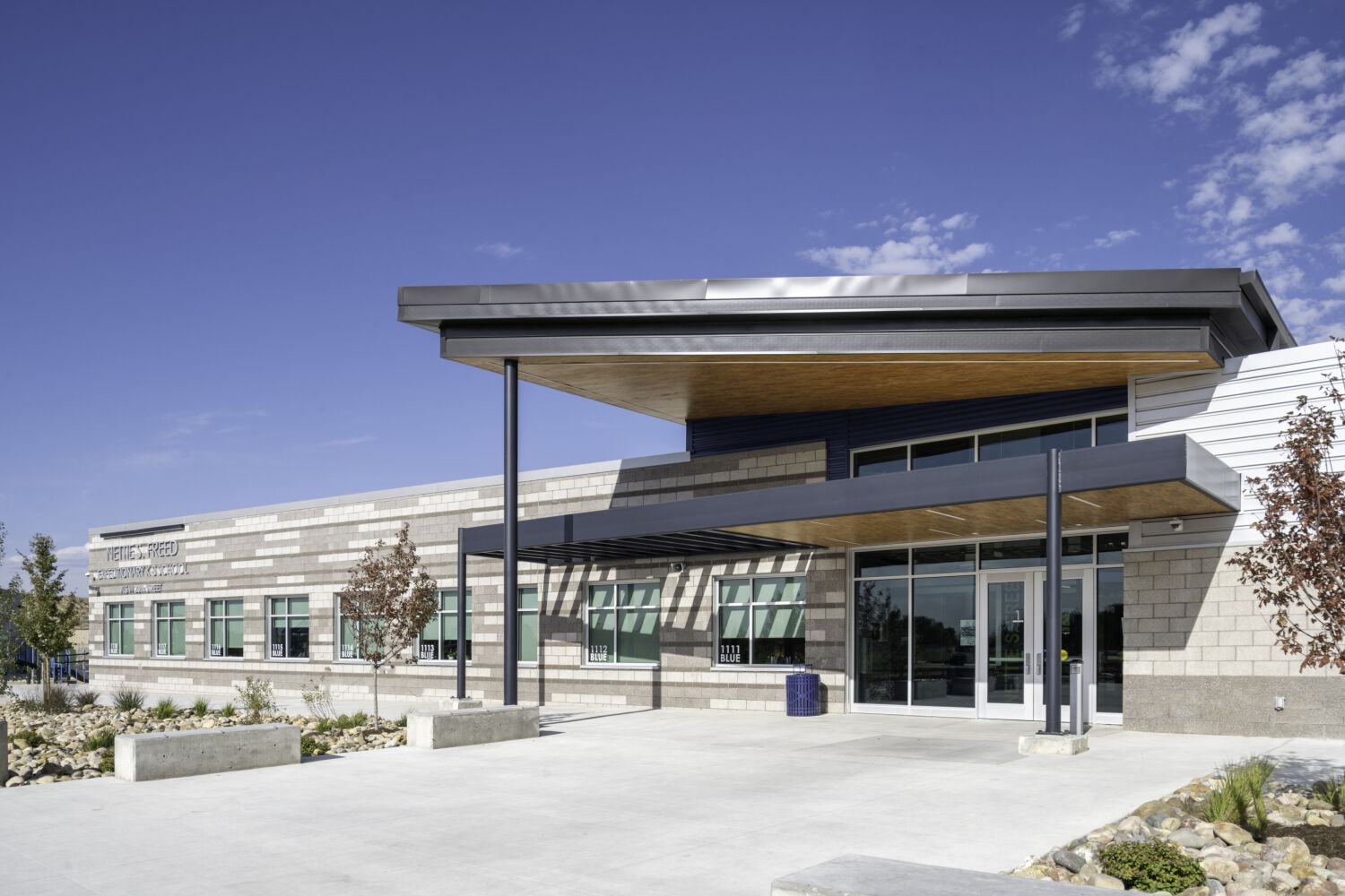 Main entrance of Nettie S. Freed Expeditionary K–8 School with a glazed entry, wood‑accent canopy, brick facade, and landscaped entry plaza.