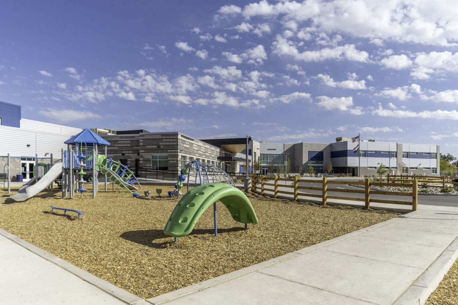 Playground at Nettie S. Freed Expeditionary K–8 School with climbing structures, slides, balance elements, and a fenced play area adjacent to the school building.