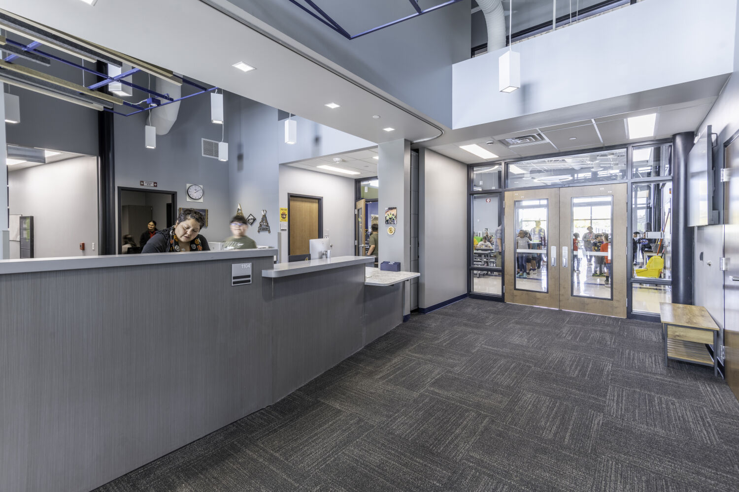 Secure school vestibule with a reception desk, controlled access doors, glazed partitions, and integrated ceiling lighting.