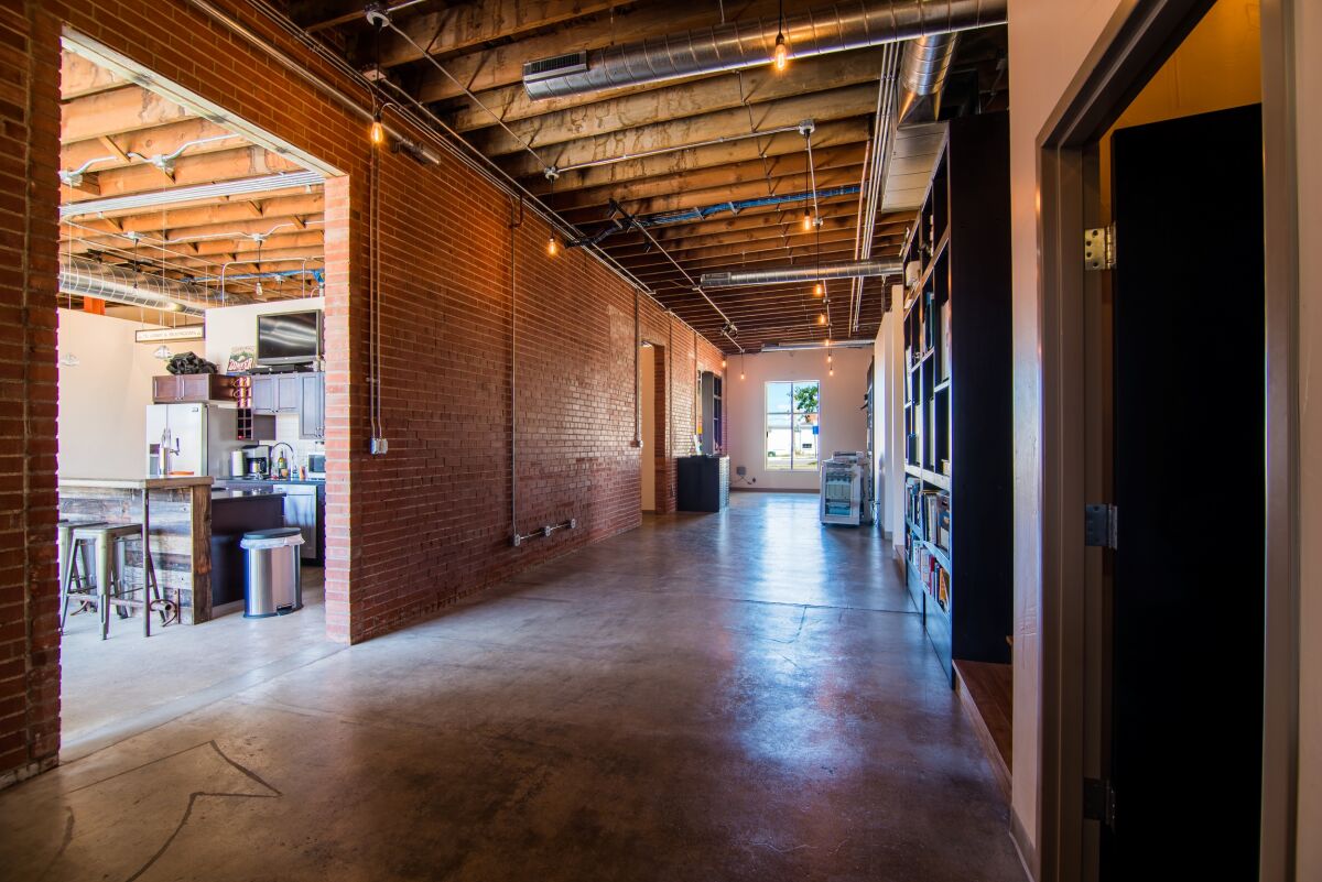 Interior corridor with polished concrete floors, exposed wood ceilings with ductwork, brick accent walls, built‑in shelving, and views into adjacent office and kitchen areas.