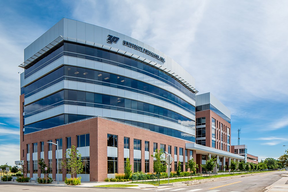 Exterior view of a multi‑story medical office building with curved glass façades, brick lower levels, and landscaped street frontage under a bright sky.