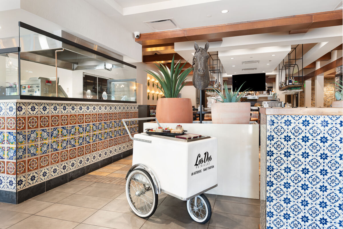 Entrance of Los Dos Potrillos featuring a tiled tortilla station, decorative planters, a dessert cart, and warm wood ceiling beams.