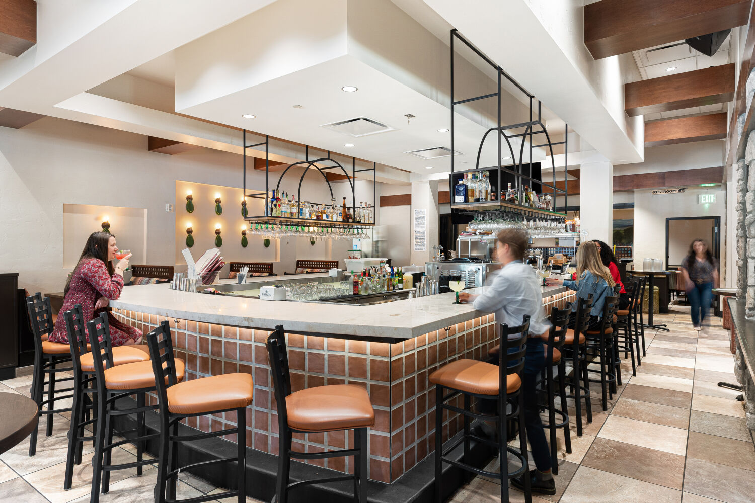 Restaurant bar area with tiled counter, high-top seating, and patrons enjoying drinks.