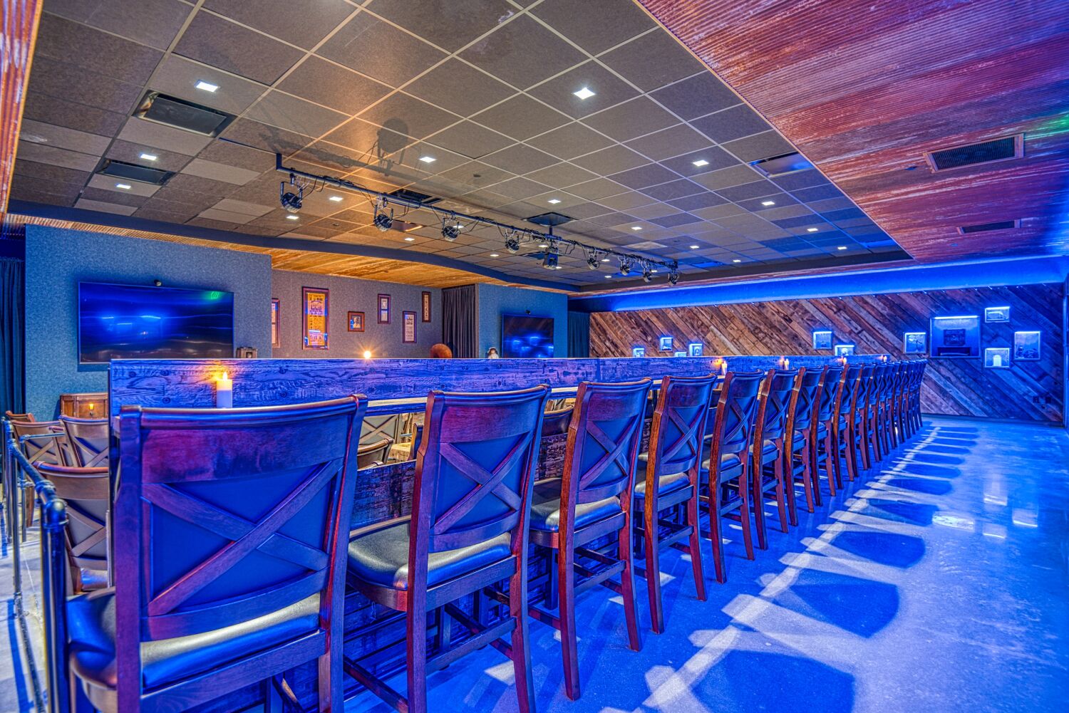 Interior seating area at Aiden Sinclair’s Underground featuring long rows of high‑back chairs, a raised platform, wood‑accent walls, and overhead theatrical lighting.