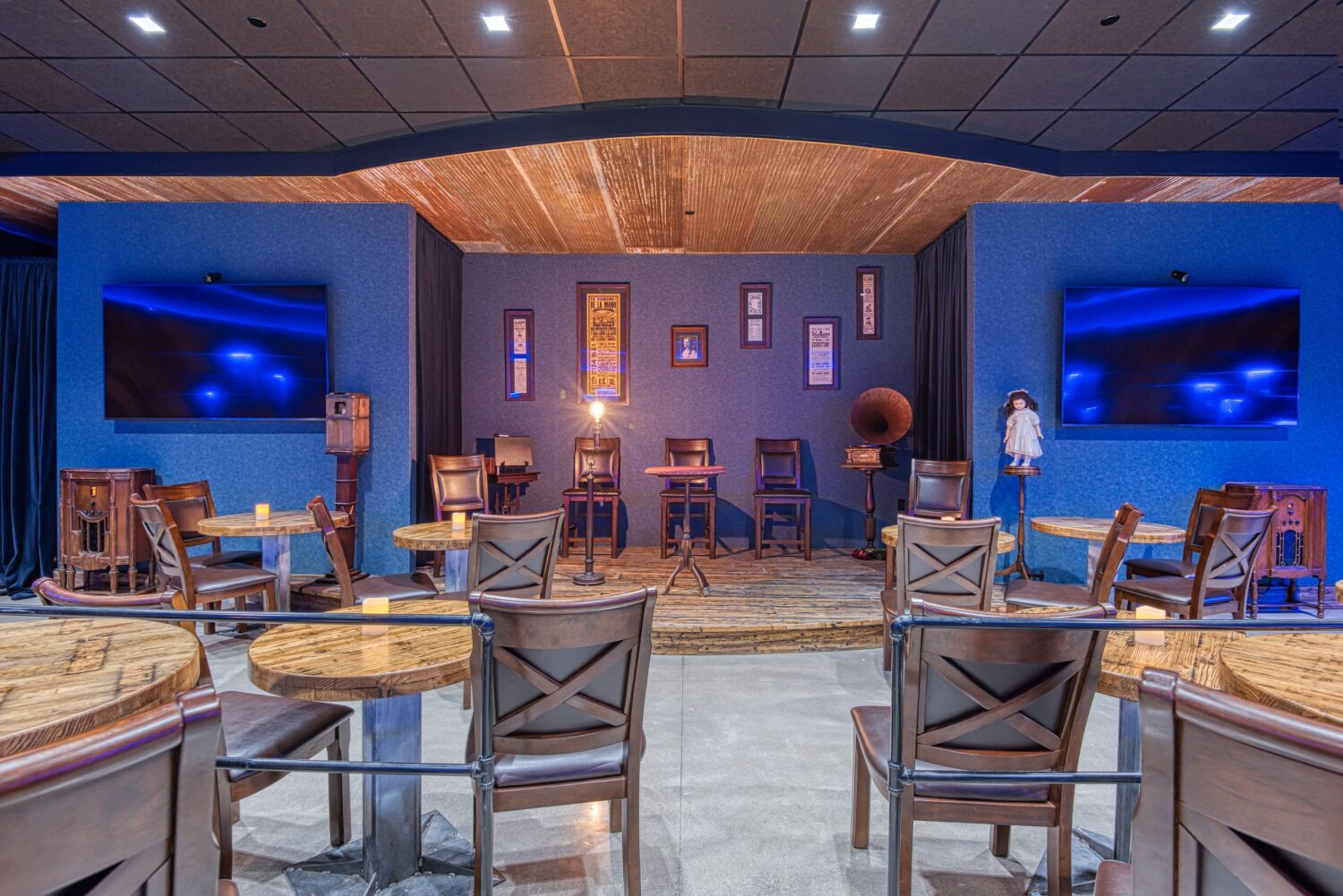 Stage area inside Aiden Sinclair’s Underground with wooden tables, arranged seating, framed posters on the wall, and theatrical lighting.