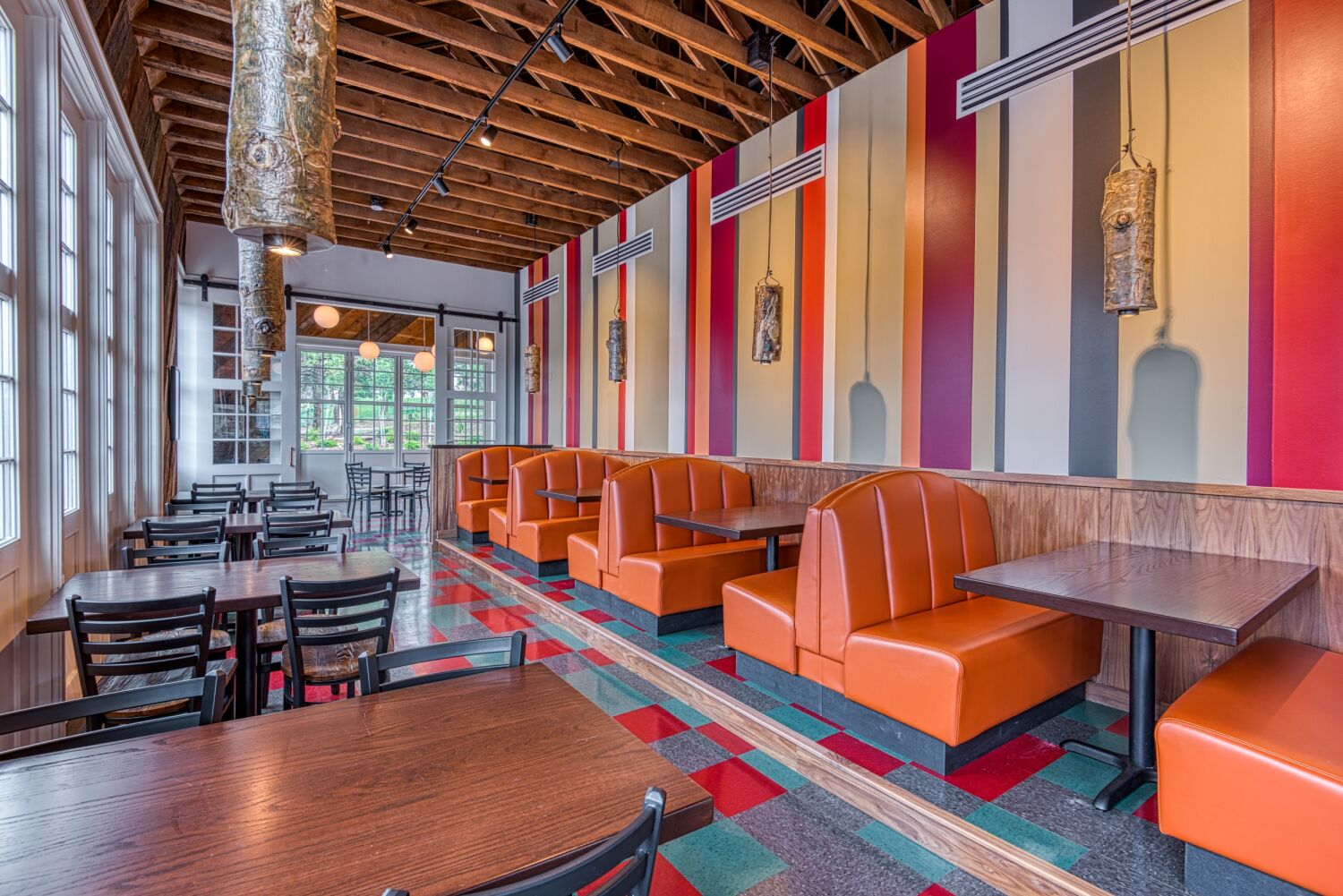 Interior of The Post restaurant featuring orange booth seating, colorful vertical wall panels, exposed wood ceiling, and patterned red‑and‑green flooring.