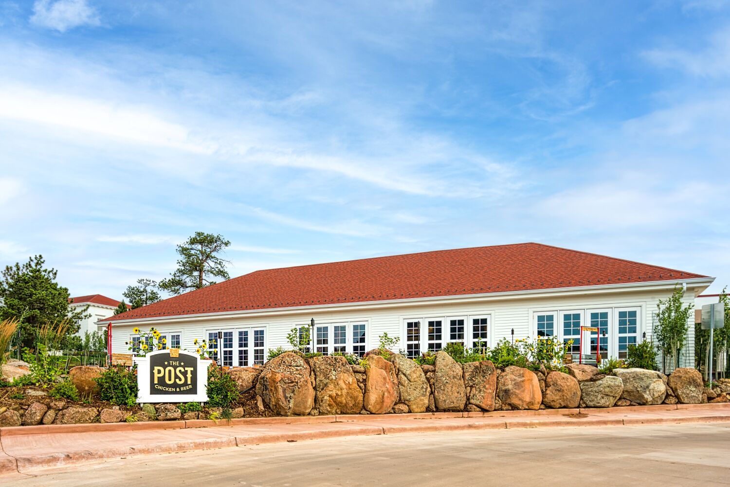 Wide exterior view of the carriage house with white siding, red roof, and stone-lined landscaping under a blue sky.