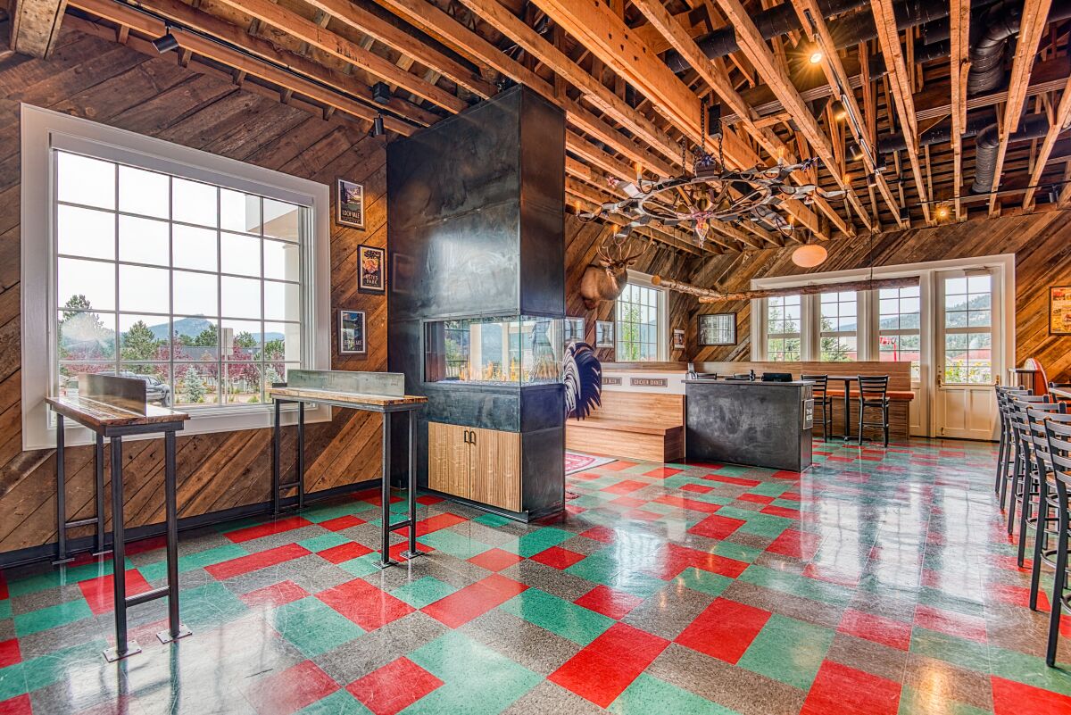 Entrance area of The Post restaurant featuring a central fireplace, exposed wood ceiling, patterned flooring, and large windows overlooking the landscape.