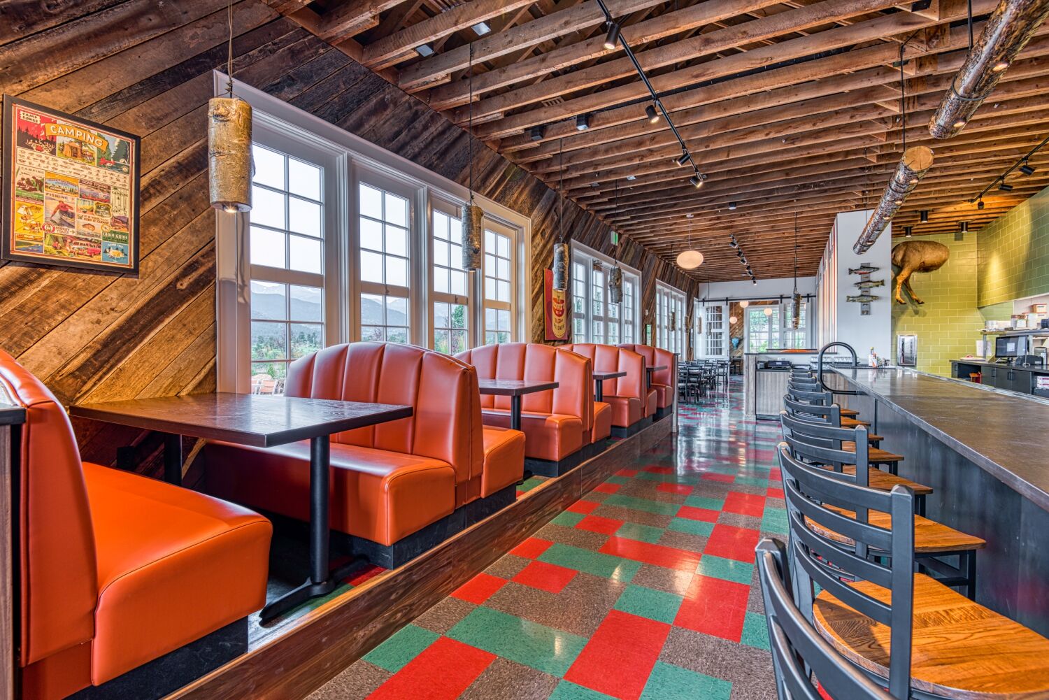 Interior of The Post restaurant featuring orange booth seating, wood‑clad walls, exposed ceiling structure, and patterned red‑and‑teal flooring.
