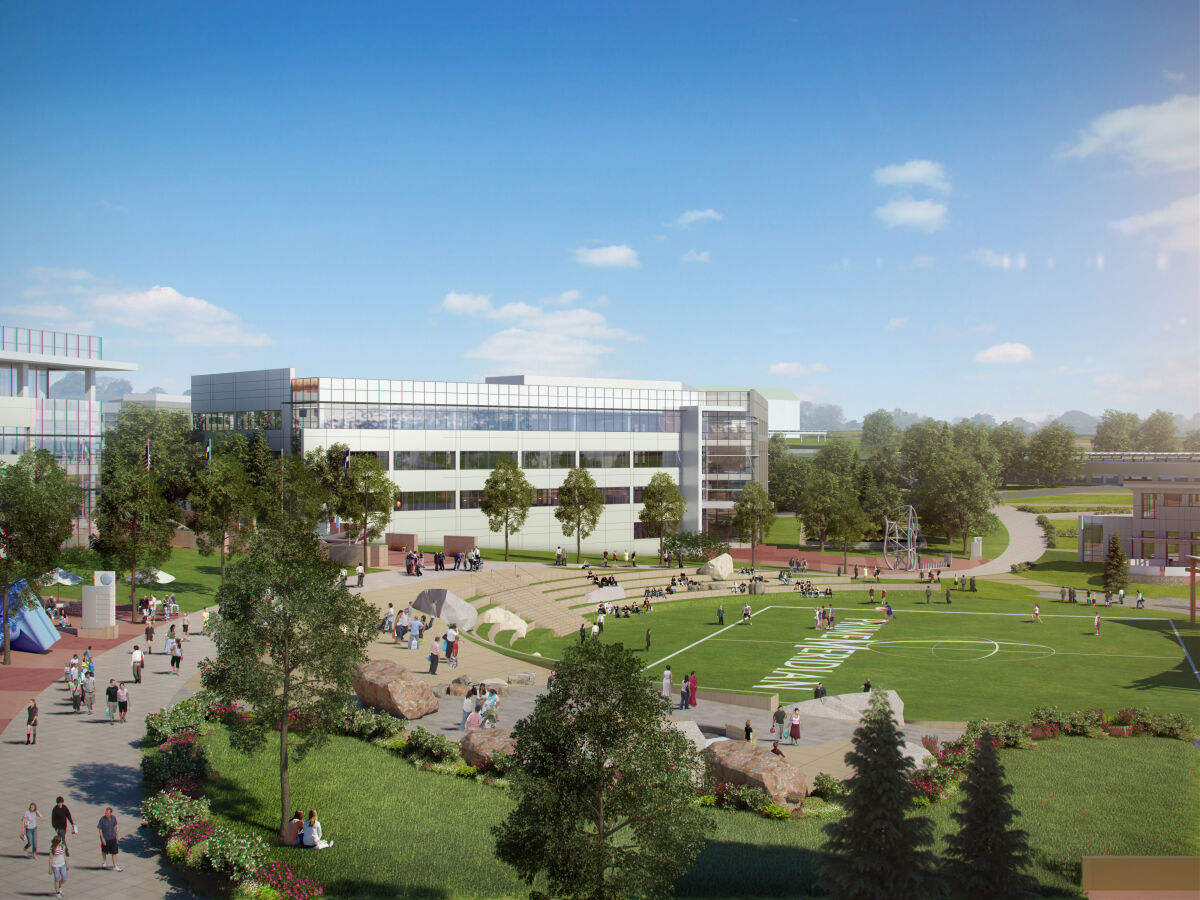 Ground‑level view of a landscaped campus green with walking paths, seating terraces, and a modern glass‑front building in the background.