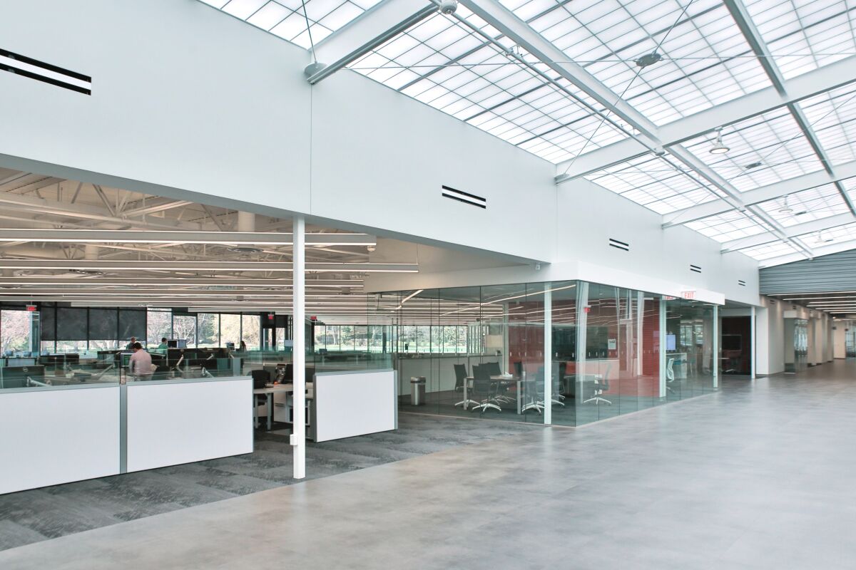 Woodward Drake bright open office area with glass‑walled meeting rooms, low workstations, and a large skylight ceiling that brings in natural light.