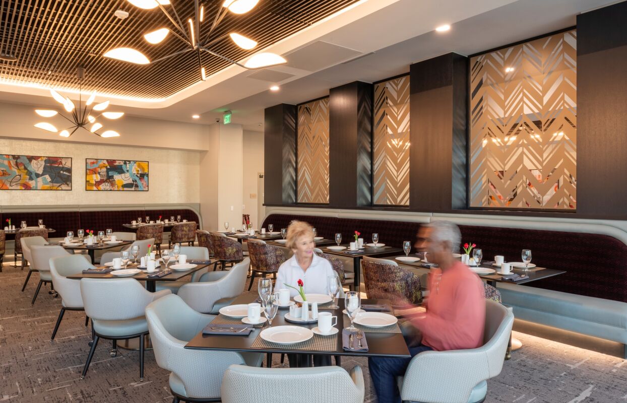 Contemporary dining room with upholstered chairs, patterned banquettes, modern light fixtures, decorative wall panels, and set tables arranged throughout the space.
