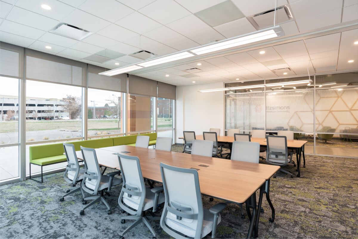 Meeting room with long tables, task chairs, a glass wall with geometric film, and large windows overlooking the campus.