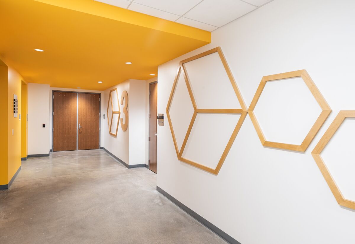 Corridor with a yellow ceiling section, wood geometric wall graphics, concrete flooring, and double doors at the end of the hall.