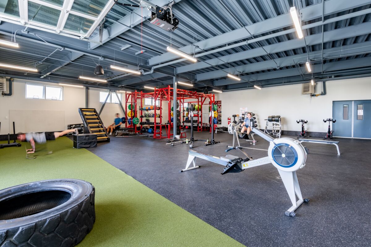 Strength training area with functional fitness equipment, weight racks, rowing machines, turf zone, and an open exposed‑ceiling structure.