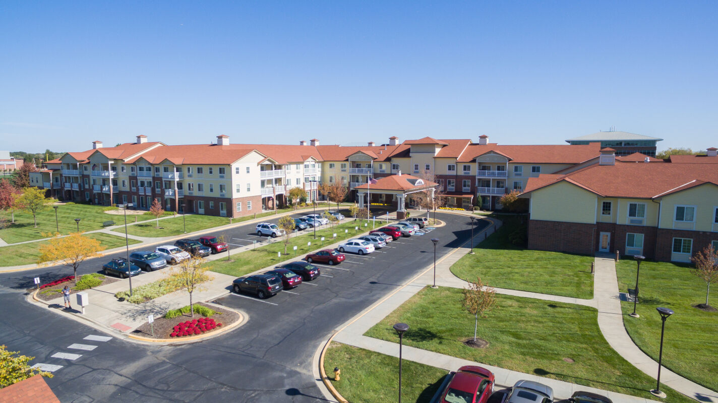 Park Meadows Senior Living campus with multi‑story residential buildings, covered entry, internal roadways, surface parking, and landscaped green spaces.