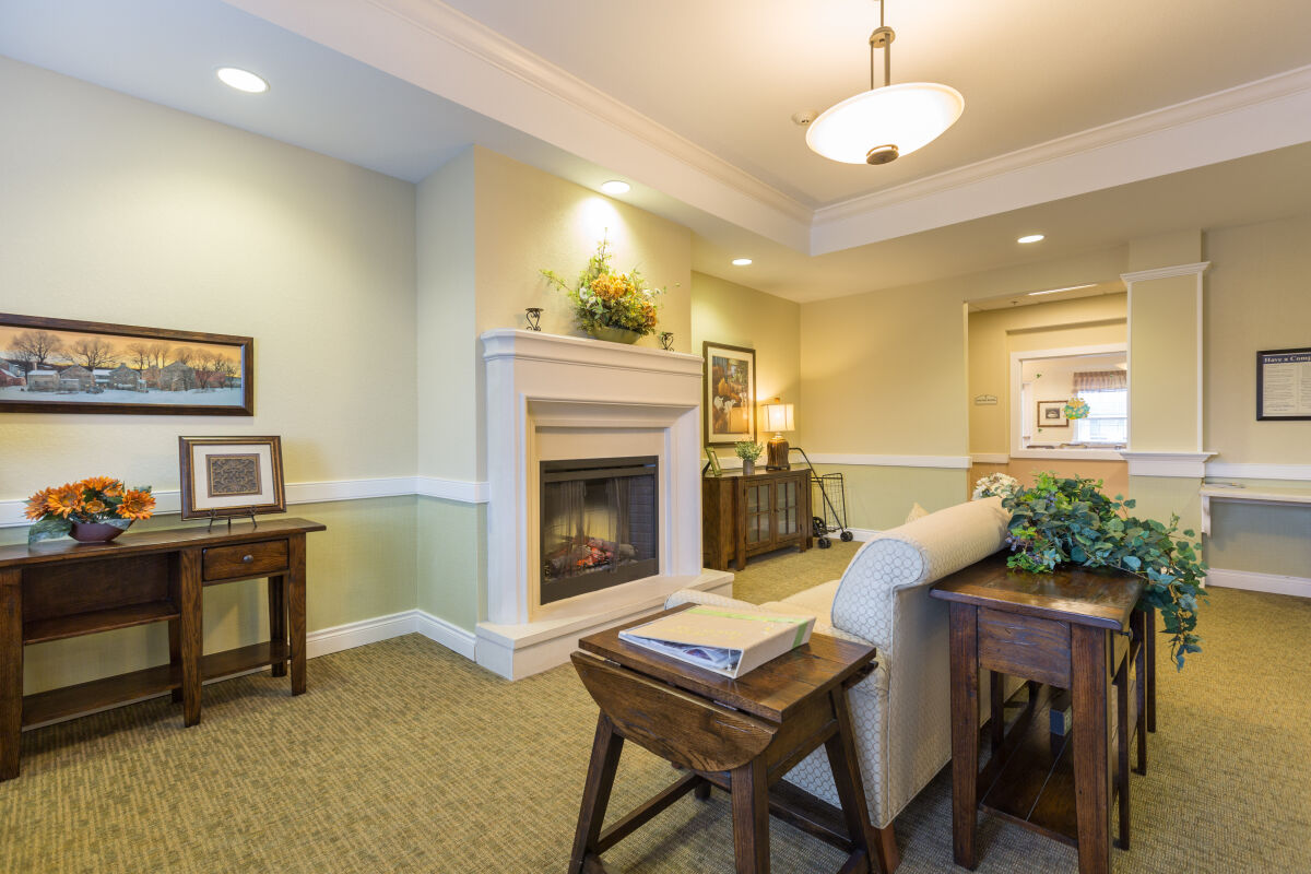 Community lounge at Park Meadows Senior Living with a fireplace, seating areas, side tables, decorative plants, and soft ambient lighting.