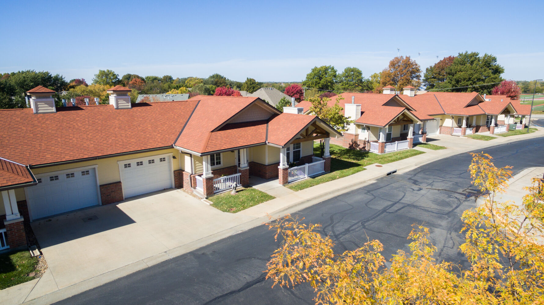 Cottage neighborhood at Park Meadows Senior Living with single‑story residential units, covered front porches, attached garages, internal street circulation, and landscaped lawns.