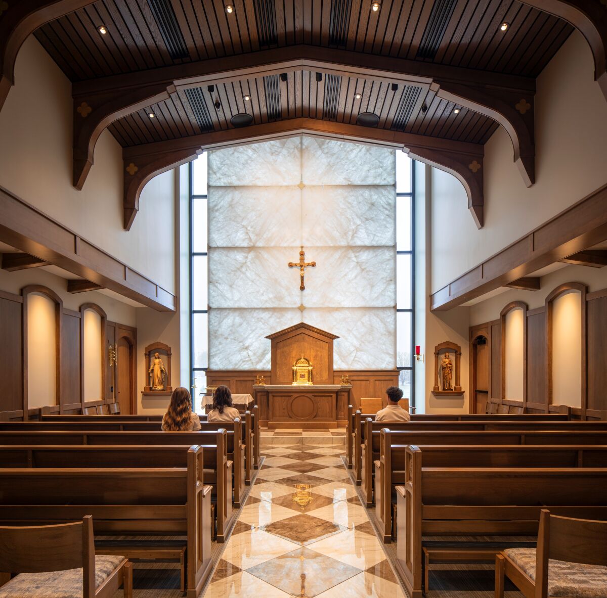 Chapel interior with wood‑beam ceiling, marble accent wall, central altar, wooden pews, and religious iconography along the side walls.