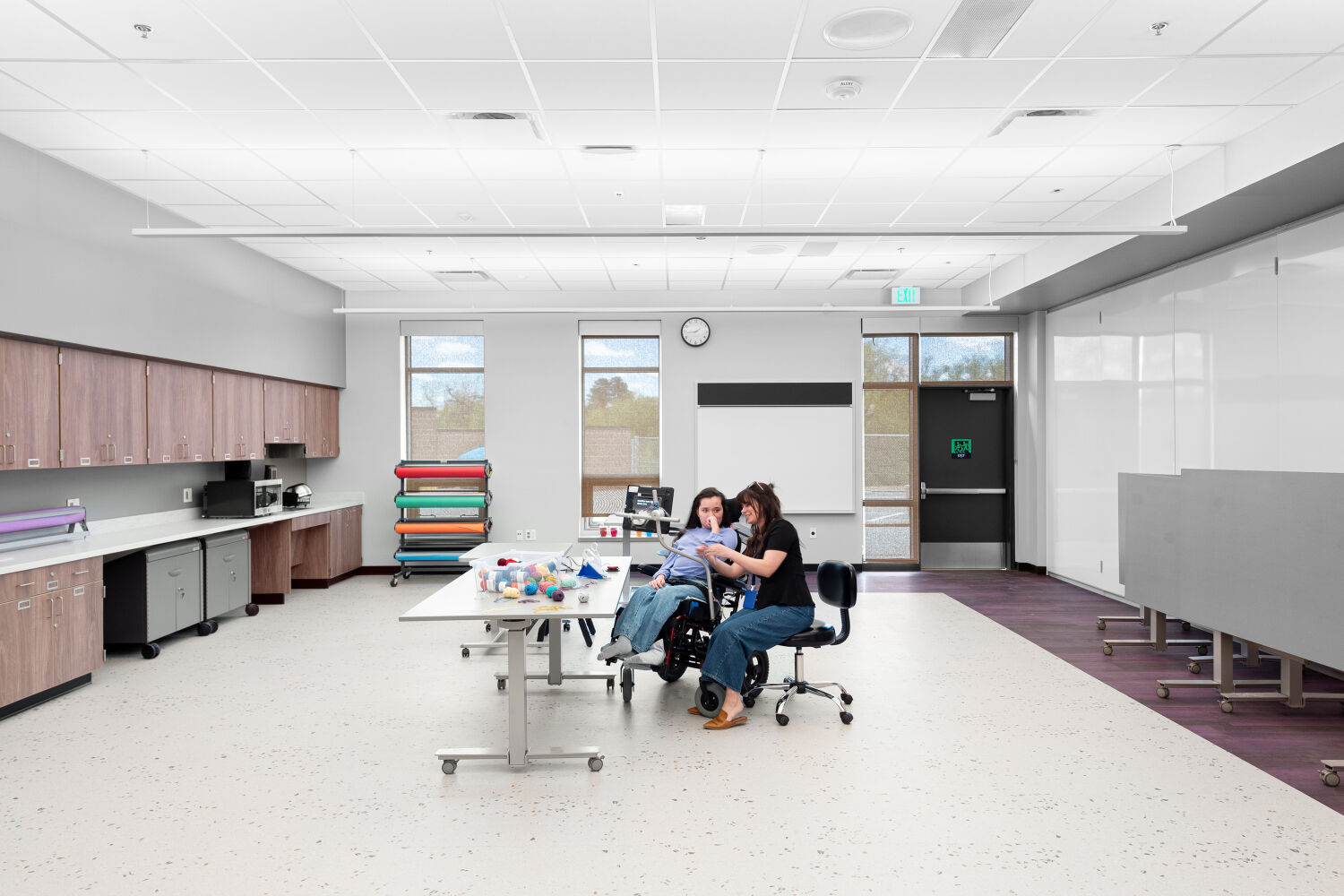 Art classroom with mobile worktables, perimeter cabinetry and sinks, open floor area for instruction, whiteboard wall, and resilient flooring.