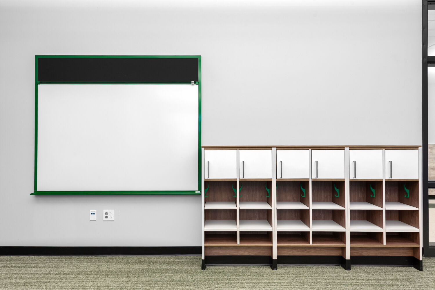 Custom student cubbies with open storage compartments, integrated coat hooks, wood finishes, and upper cabinet doors along a classroom wall.