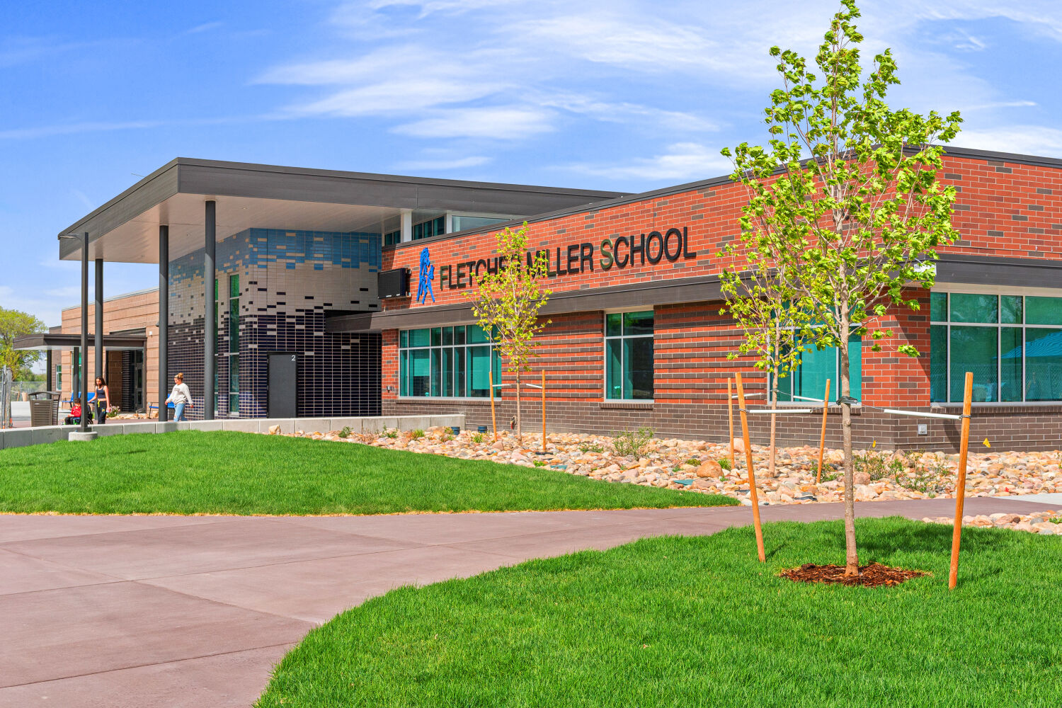 Main entrance of Fletcher Miller School with a brick facade, school signage, glazed windows, covered entry canopy, and landscaped lawn and walkway.