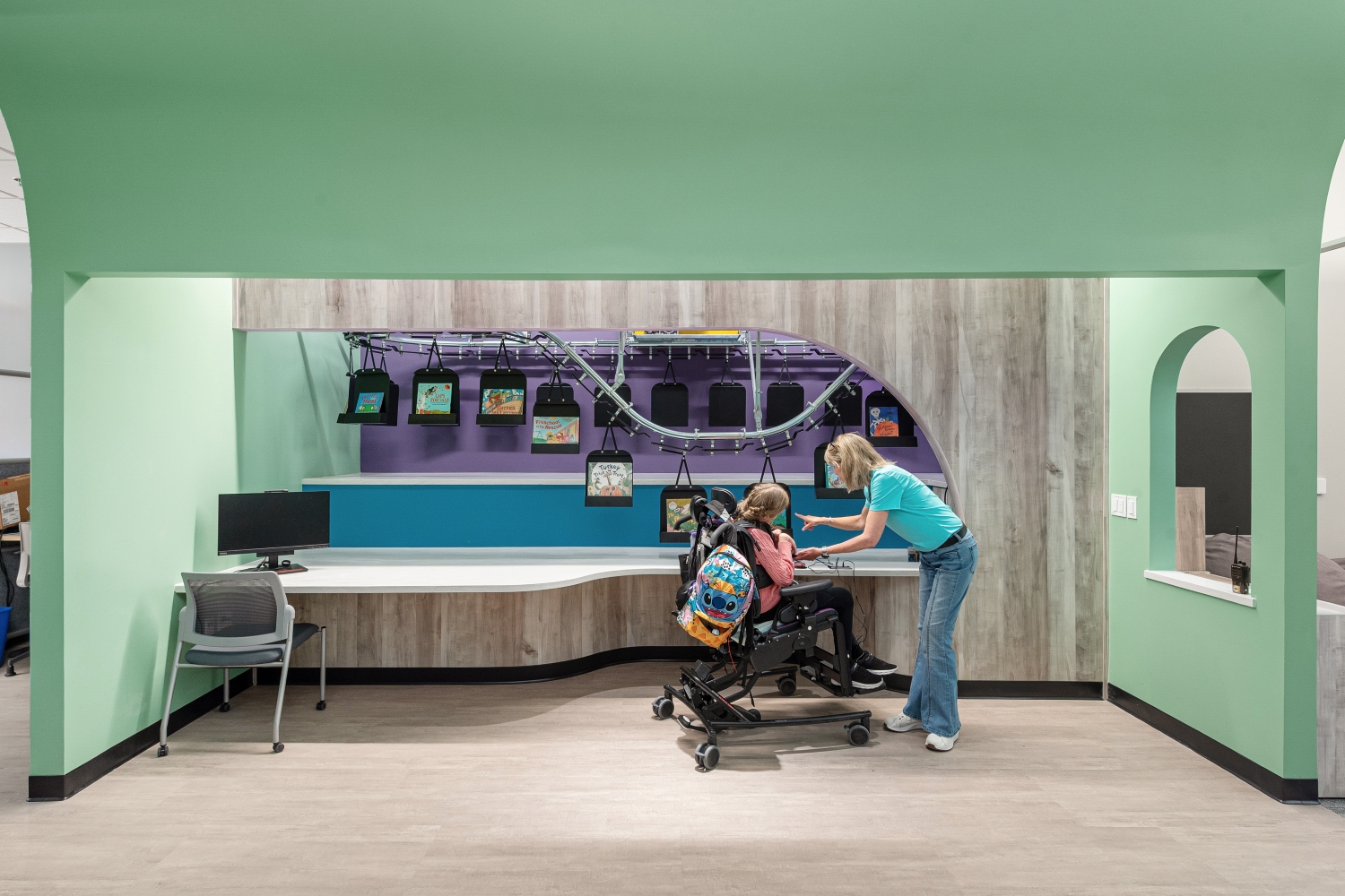 Library service desk with an overhead book conveyor system, integrated shelving, curved millwork counter, and adjacent reading and circulation areas.