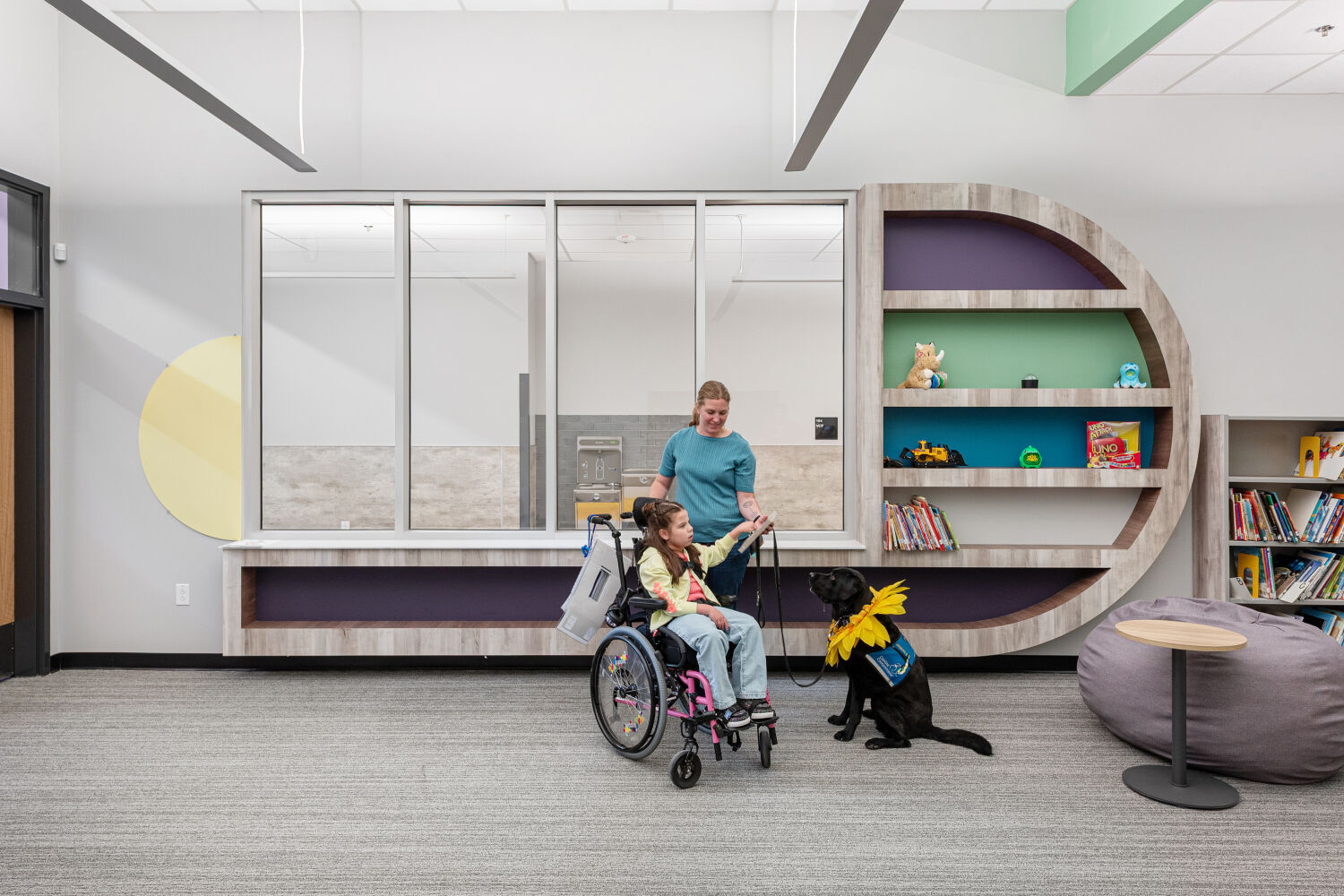 Custom library shelving with curved millwork, integrated display niches, low book storage, and adjacent soft seating within the learning commons.